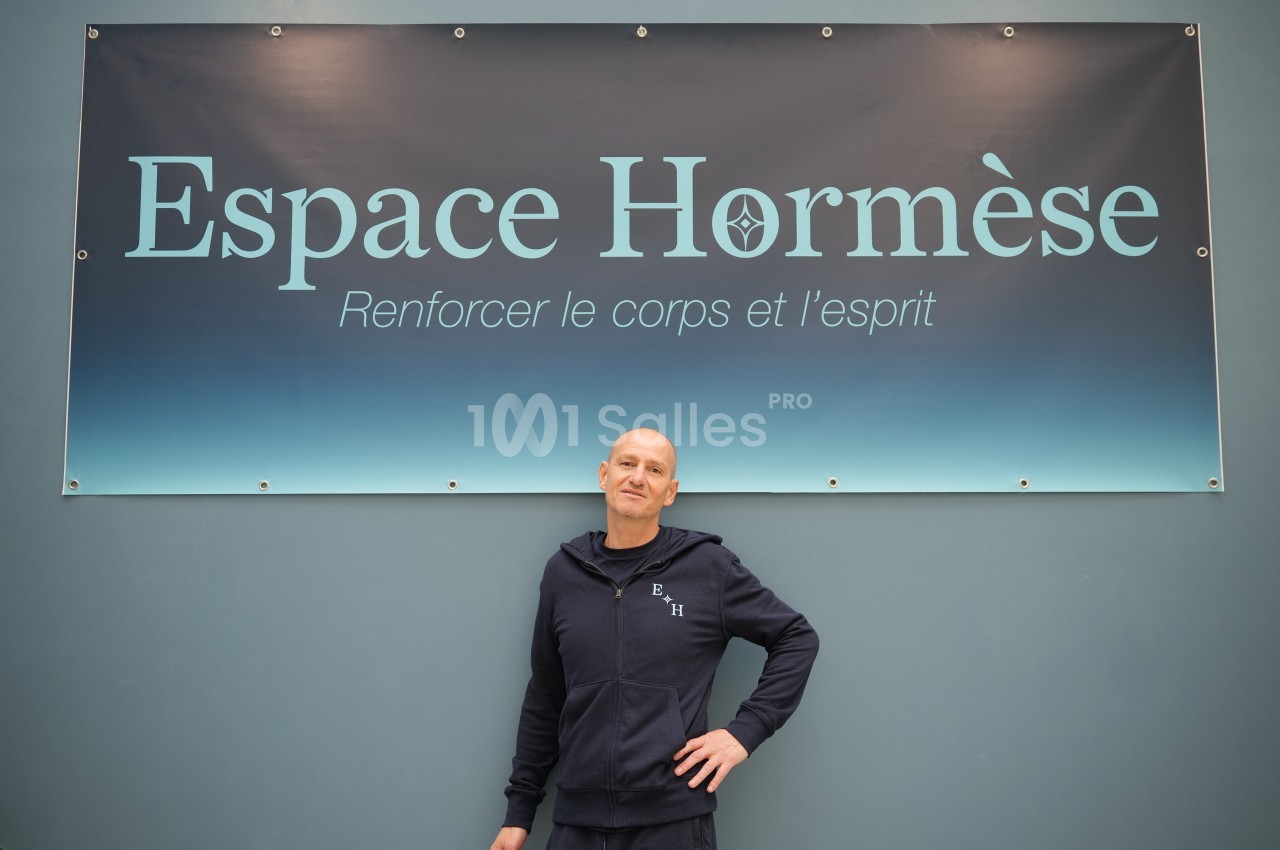 Un homme en tenue sportive pose devant une affiche indiquant ’Espace Hormèse, Renforcer le corps et l'esprit’.