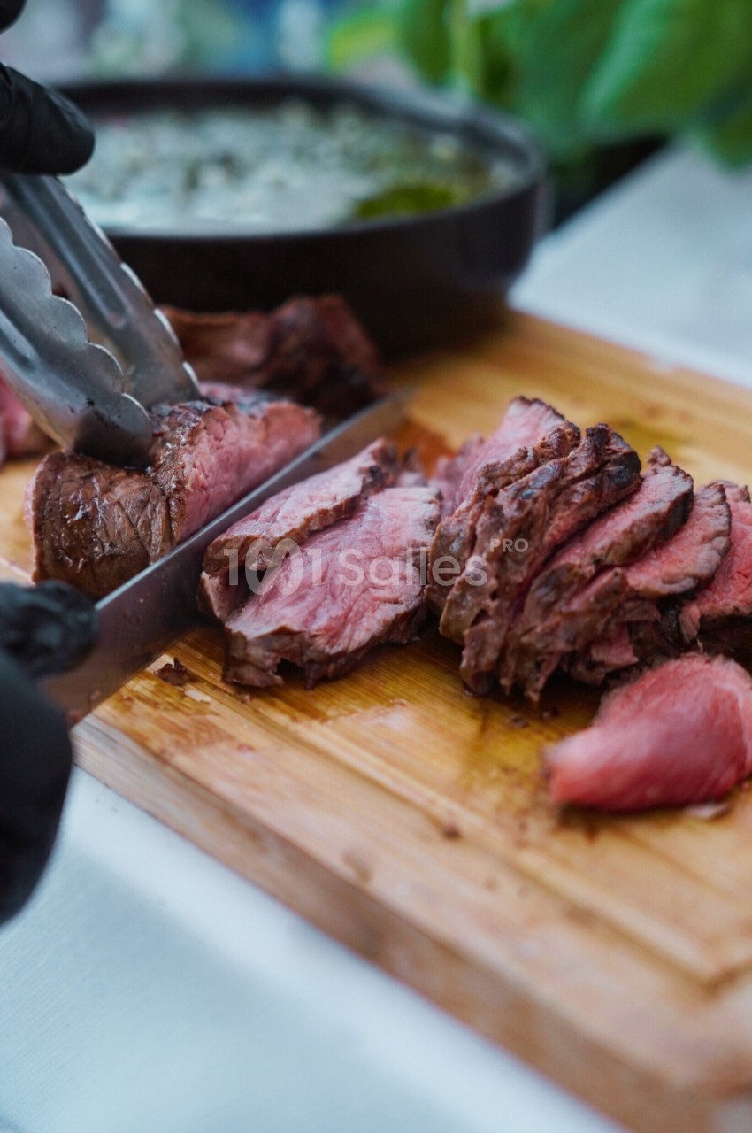 Tranches de viande rouge juteuse découpées sur une planche en bois avec une pince et un couteau.