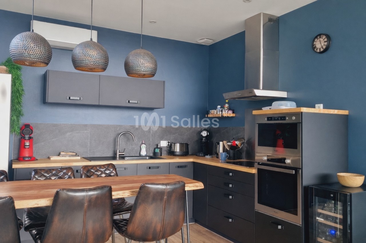 Cuisine moderne avec murs bleus, meubles noirs, plan de travail en bois, électroménagers intégrés et table avec chaises.