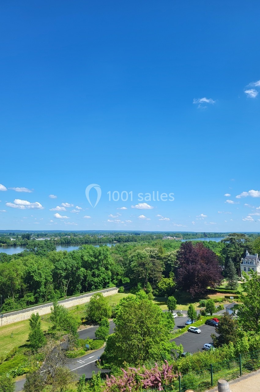 Vue panoramique sur un parc verdoyant avec des arbres, une route, un bâtiment et un ciel bleu dégagé.