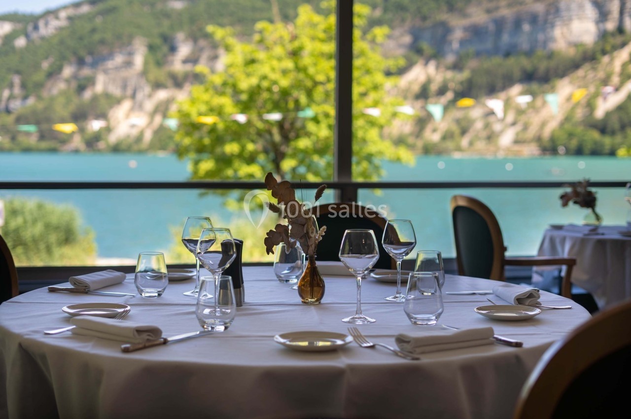 Table dressée avec élégance dans un restaurant, vue sur un lac entouré de collines verdoyantes en arrière-plan.