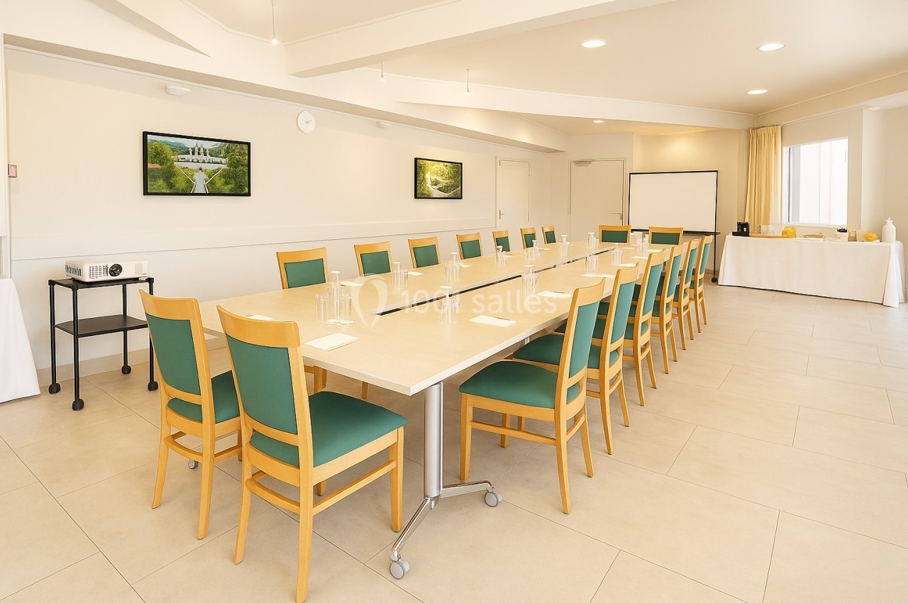Salle de réunion lumineuse avec une grande table rectangulaire entourée de chaises vertes et équipements de présentation.