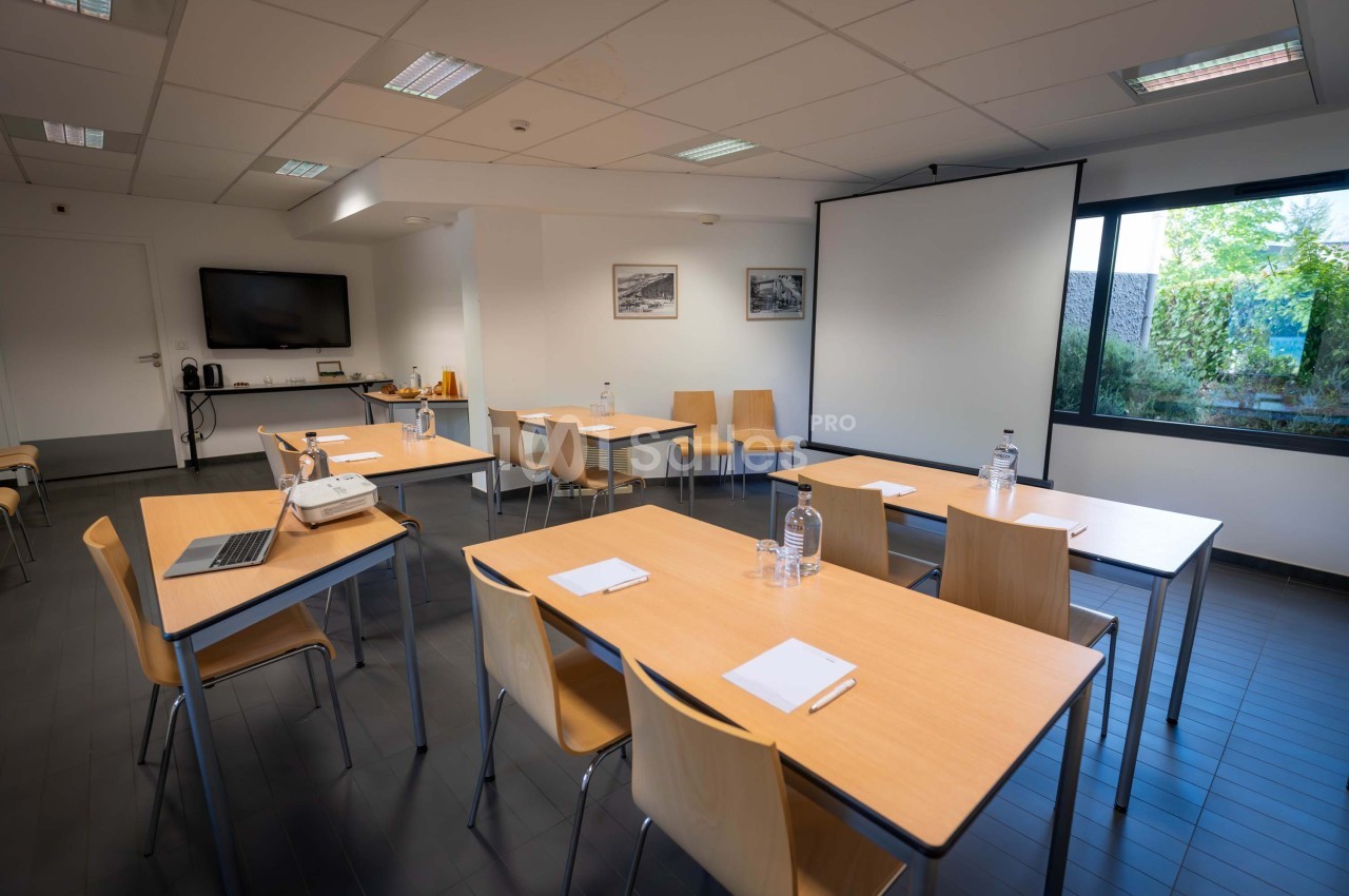 Salle de réunion lumineuse avec tables en bois, chaises, projecteur, écran blanc et vue sur un jardin.
