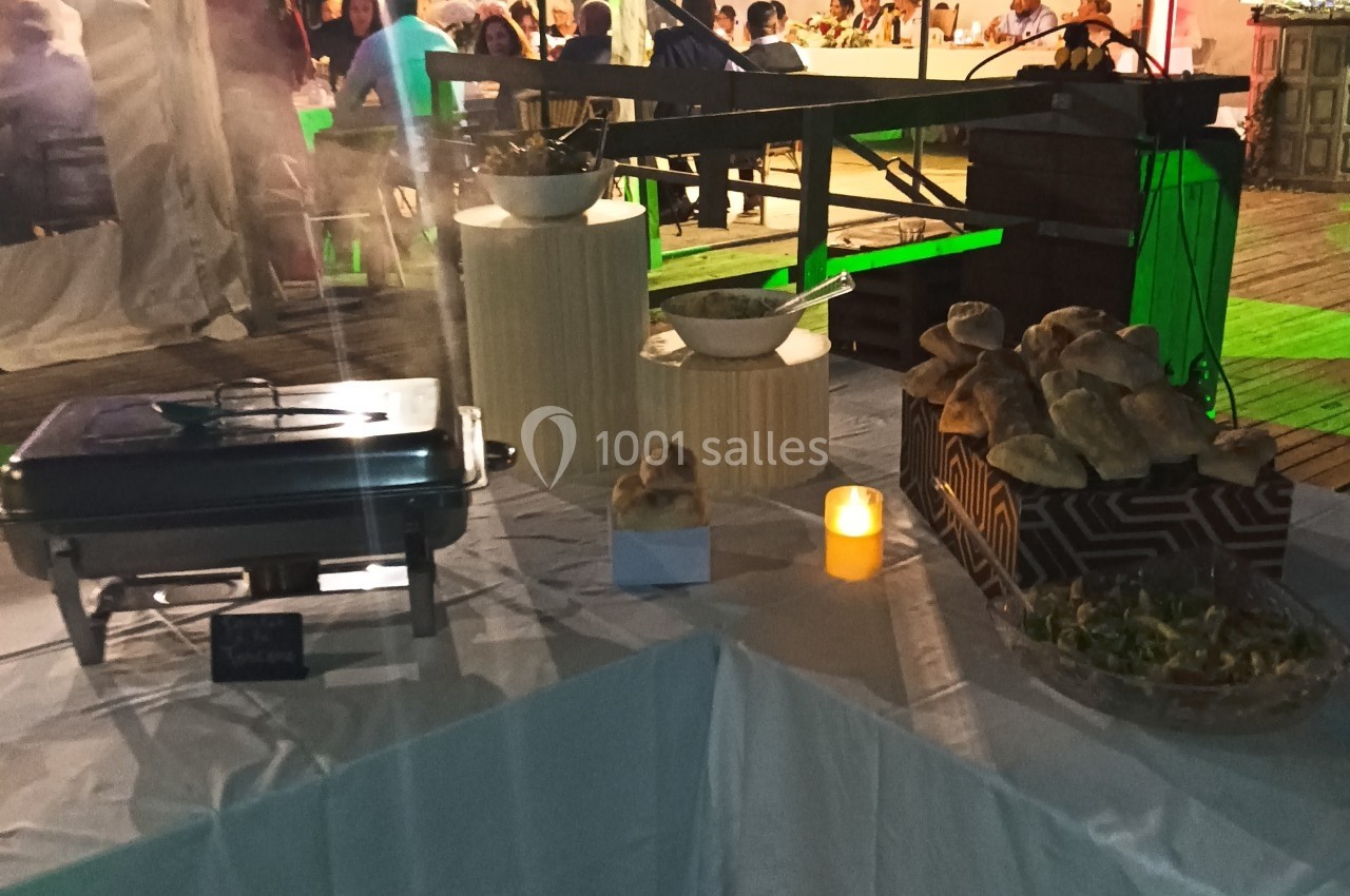 Buffet avec plats chauds, pains et salades disposés sur une table blanche, éclairée par une bougie.