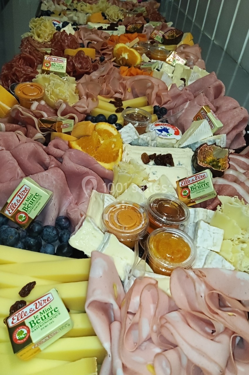 Plateau garni de charcuteries, fromages, fruits frais, confitures et beurre, présenté sur une longue table.