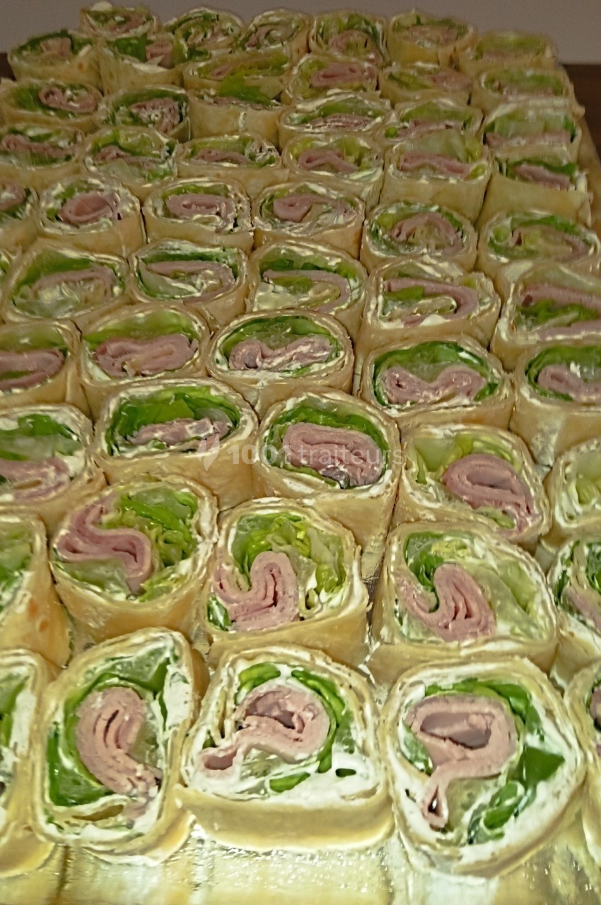 Plateau de roulés apéritifs garnis de salade, viande et fromage, disposés en rangées serrées.