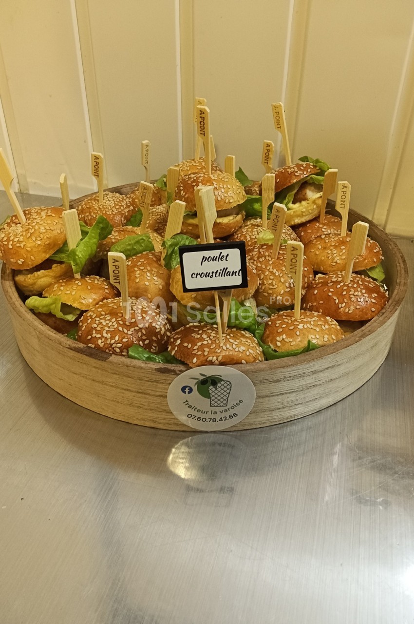 Plateau de mini-burgers au poulet croustillant avec salade, servis avec des piques en bois, sur une table en inox.
