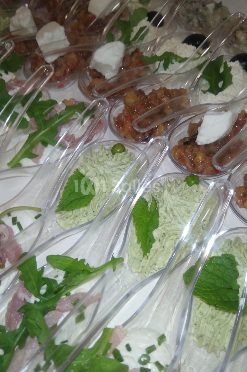 Assortiment de verrines et cuillères apéritives garnies de mousse verte, fromage, légumes et herbes fraîches.
