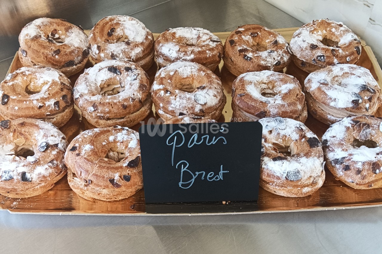 Plateau de Paris-Brest garnis de crème, saupoudrés de sucre glace, exposés sur un comptoir de pâtisserie.