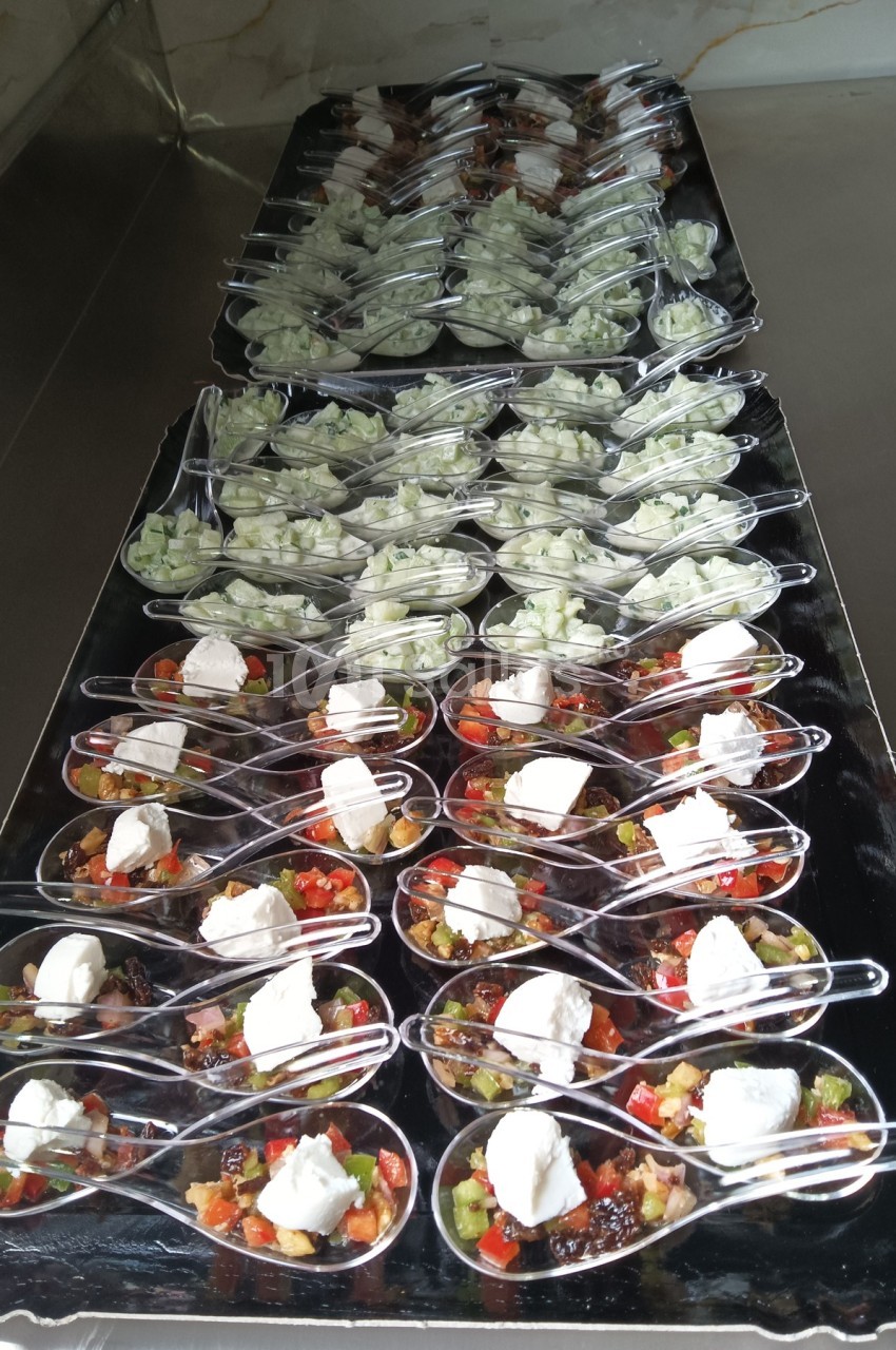 Cuillères apéritives alignées, garnies de légumes colorés, fromage frais et dés de concombre sur un plateau noir.