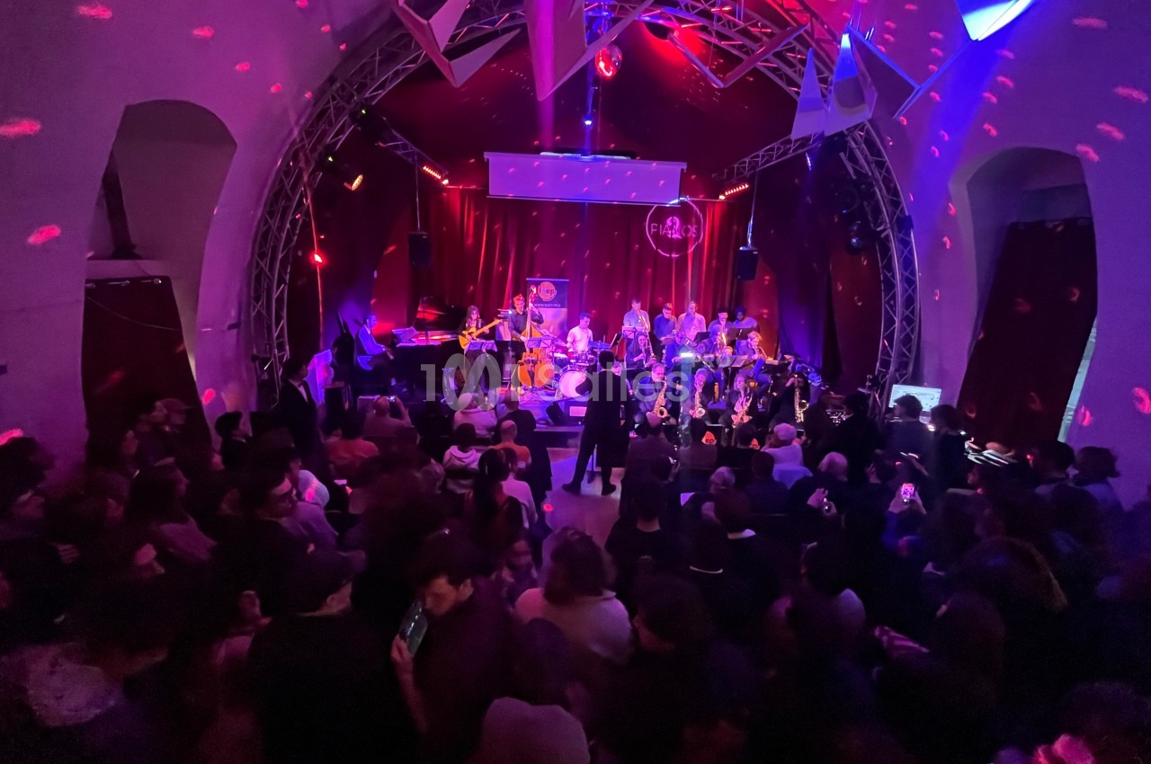 Concert en intérieur avec un groupe sur scène, éclairages colorés et public nombreux dans une ambiance festive.