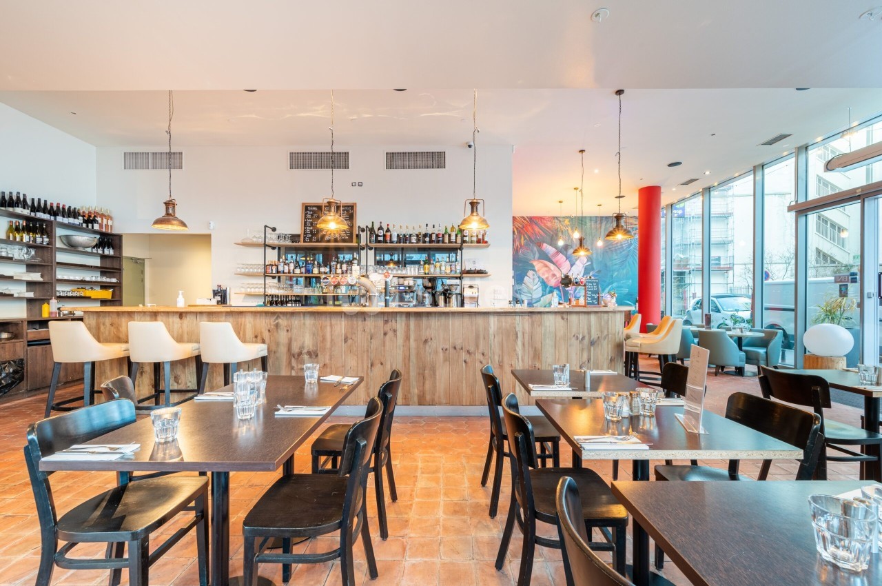 Salle de restaurant lumineuse avec tables en bois, bar central en bois clair et décoration moderne.