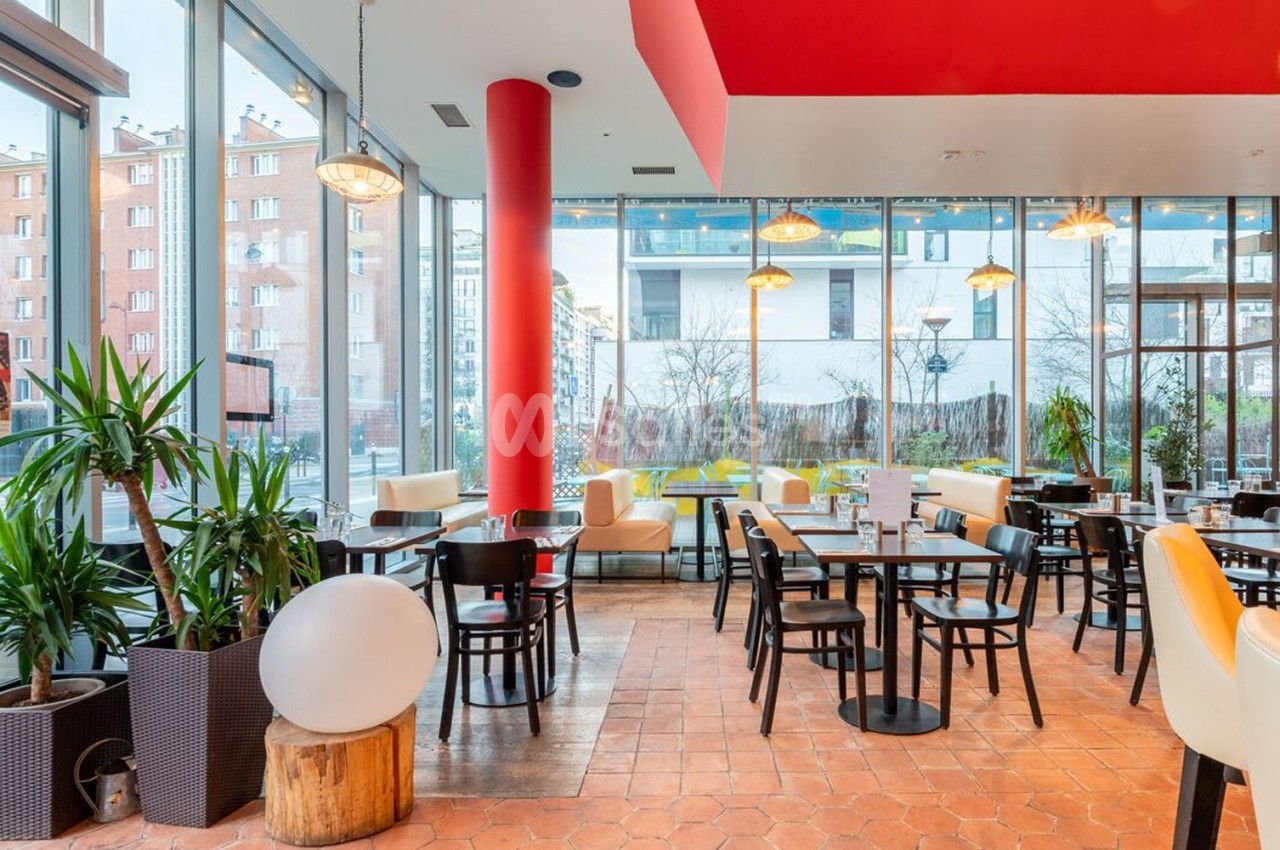 Salle de restaurant lumineuse avec grandes baies vitrées, mobilier moderne et plantes décoratives.