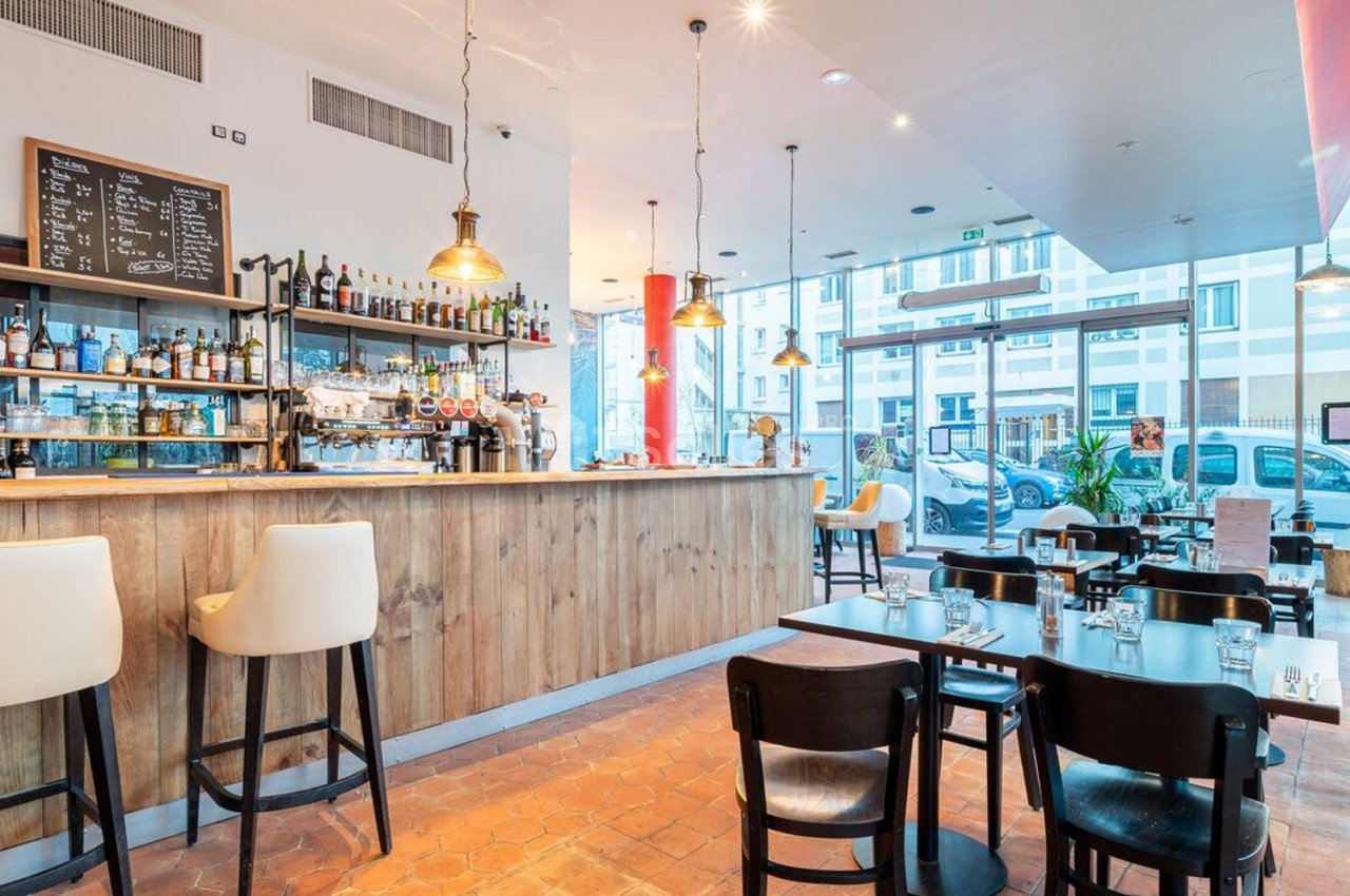 Intérieur d'un café moderne avec un bar en bois, des tables et chaises noires, éclairé par des suspensions lumineuses.