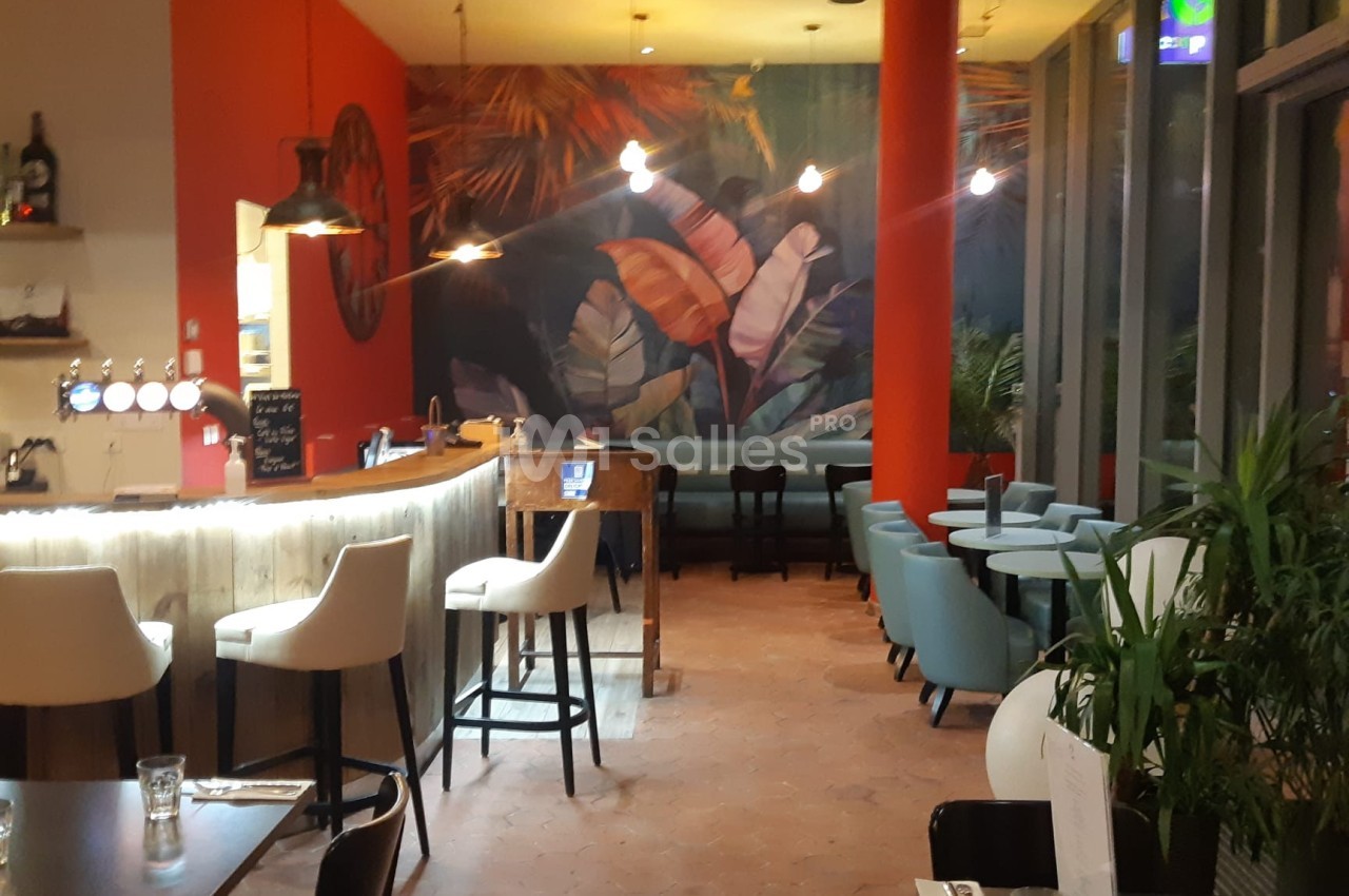 Intérieur d'un restaurant avec un bar, des tables, des chaises modernes et une fresque murale tropicale colorée.