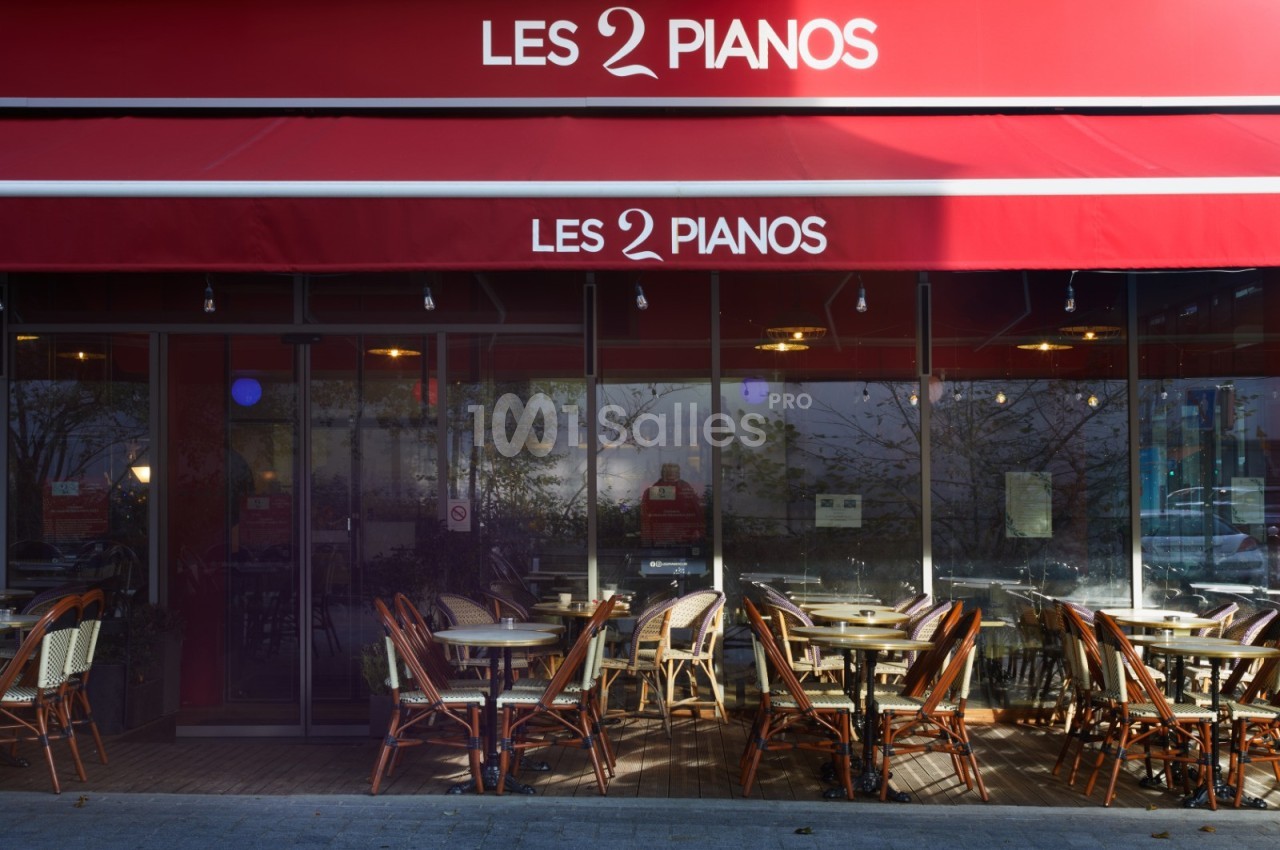 Façade d'un café-restaurant avec terrasse extérieure, tables et chaises en osier sous un auvent rouge.