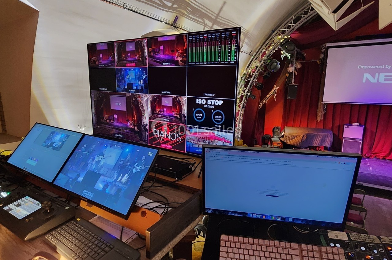 Poste de régie audiovisuelle avec plusieurs écrans et équipements, supervisant une scène dans une salle de spectacle.