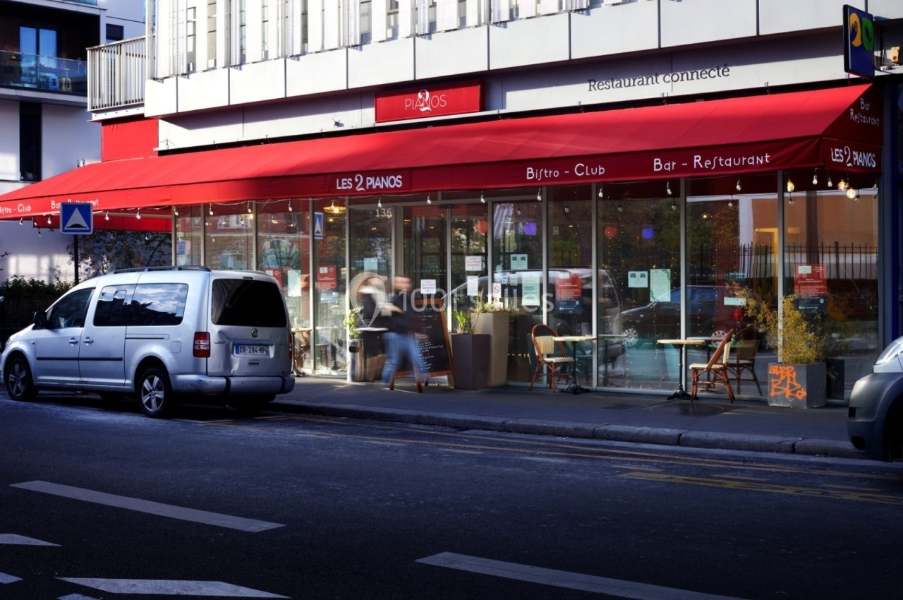 Façade d'un restaurant avec terrasse, éclairage nocturne et une voiture stationnée devant.