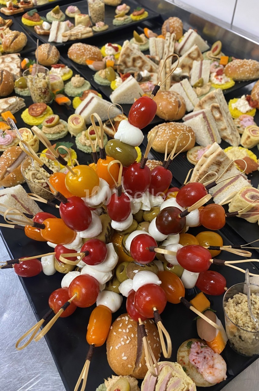 Plateau de buffet avec brochettes de tomates cerises et mozzarella au premier plan, entouré de divers amuse-bouches.