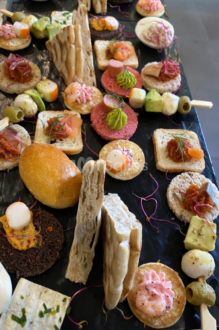 Assortiment de bouchées apéritives variées disposées sur un plateau noir, incluant pains, légumes et garnitures colorées.
