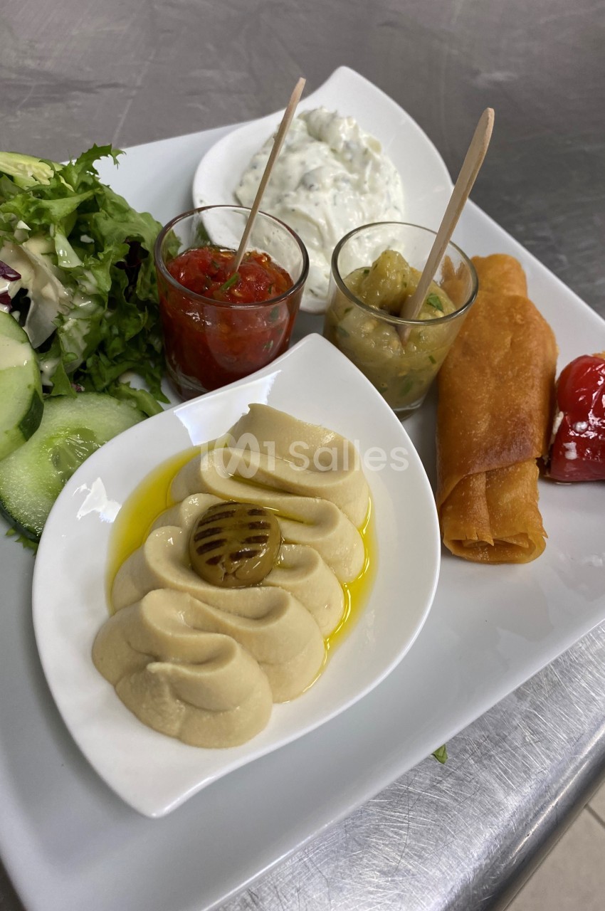 Assiette composée de houmous, sauces variées, salade verte, rouleaux croustillants et légumes grillés.