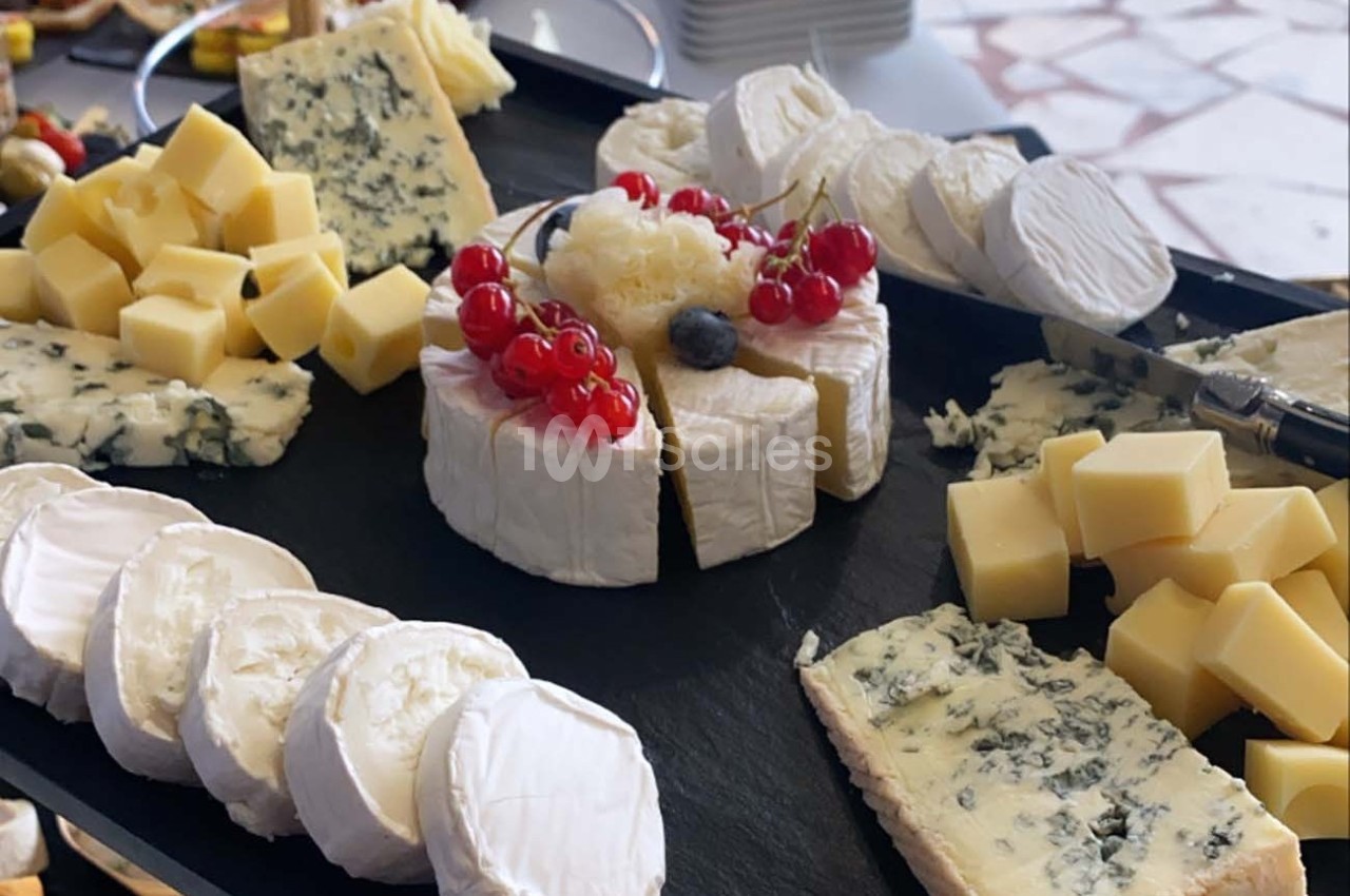 Plateau de fromages variés avec brie, bleu, morceaux de fromage à pâte dure et garniture de groseilles rouges.