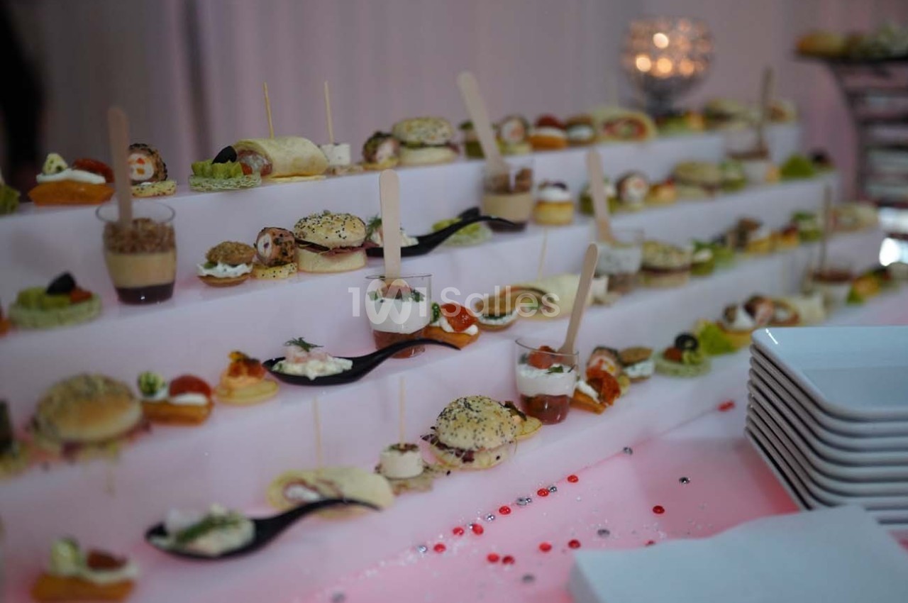 Plateau de bouchées apéritives variées présentées sur des étagères, avec des assiettes empilées à droite.