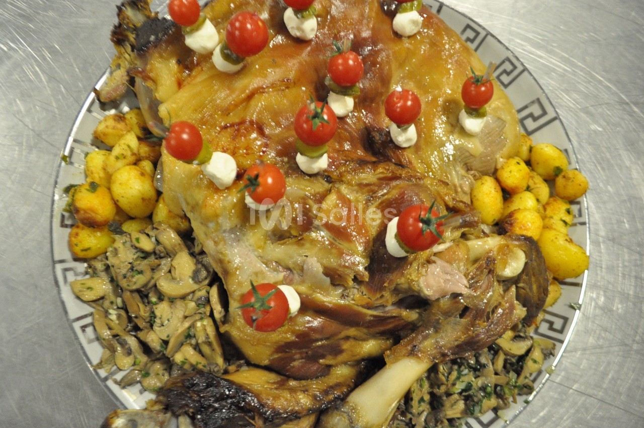 Plat de viande rôtie garni de tomates cerises, pommes de terre sautées et champignons sur un plat décoratif.