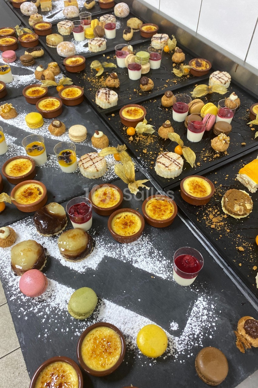Plateaux garnis de desserts variés, incluant macarons, crèmes brûlées, verrines et pâtisseries, disposés sur un plan de…
