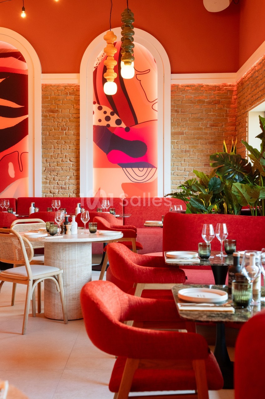 Salle de restaurant moderne avec murs en briques, décorations colorées, plantes et tables dressées.