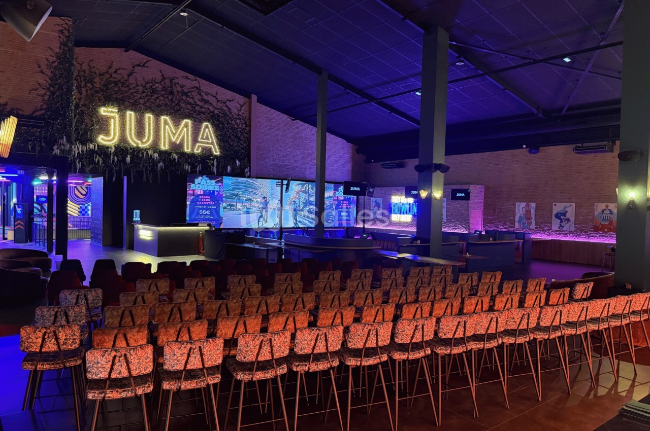 Salle aménagée avec des rangées de chaises face à une scène éclairée, dans un espace moderne et coloré.