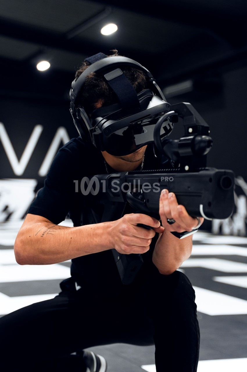 Homme portant un casque de réalité virtuelle et tenant un équipement simulant une arme dans un environnement intérieur.
