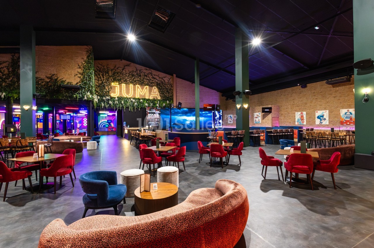 Salle spacieuse avec tables et fauteuils colorés, éclairage chaleureux, décorations murales et enseigne lumineuse ’JUMA’.