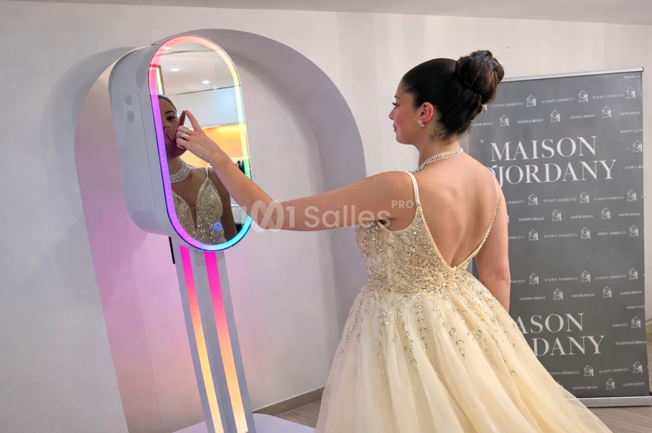 Une femme en robe de soirée beige interagit avec un miroir lumineux dans un espace intérieur.