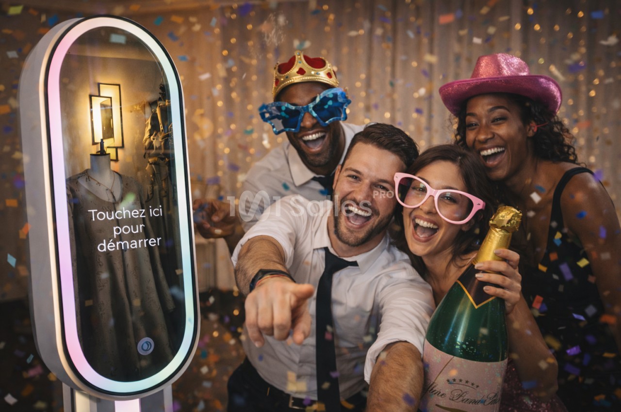Des personnes souriantes posent devant une borne photo interactive, entourées de confettis et portant des accessoires…