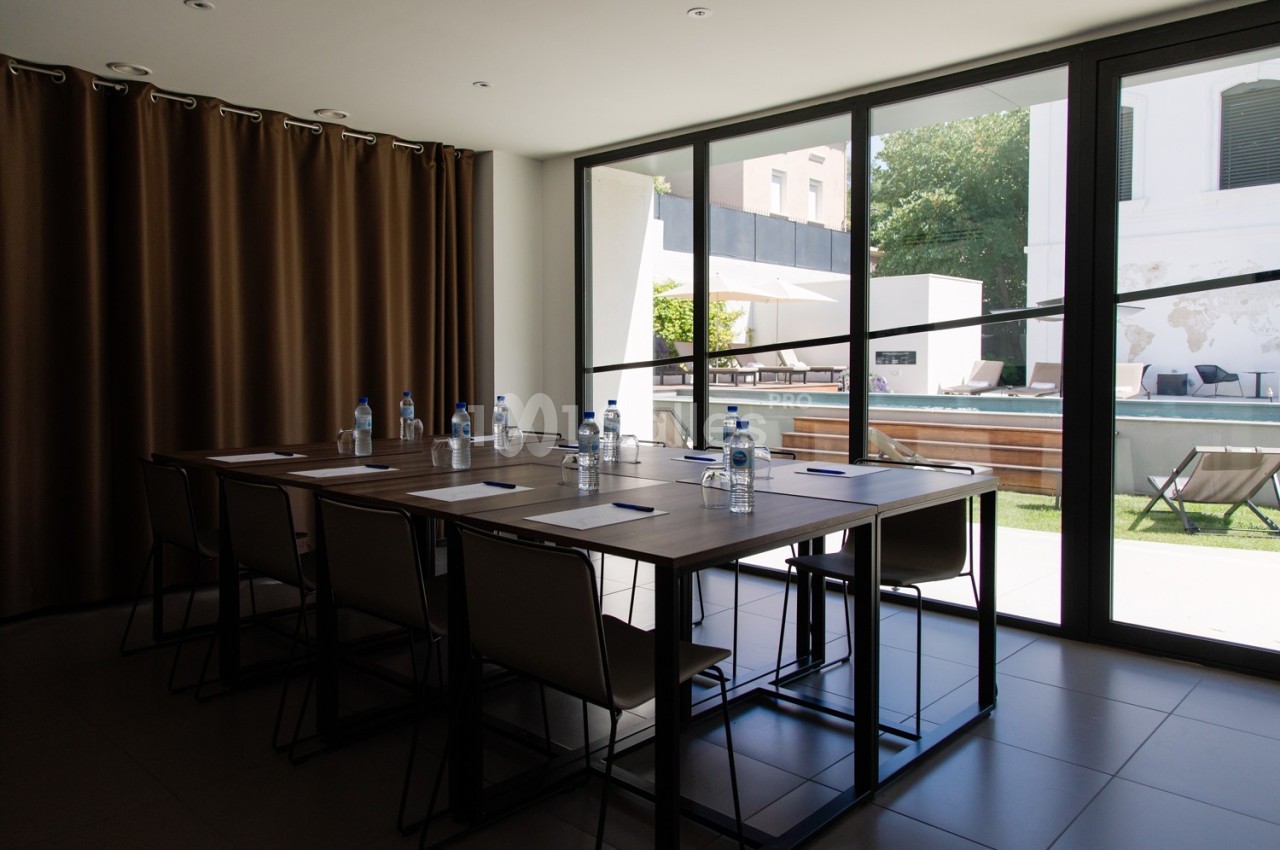 Salle de réunion lumineuse avec une grande table, des chaises, des bouteilles d'eau et vue sur une terrasse extérieure.
