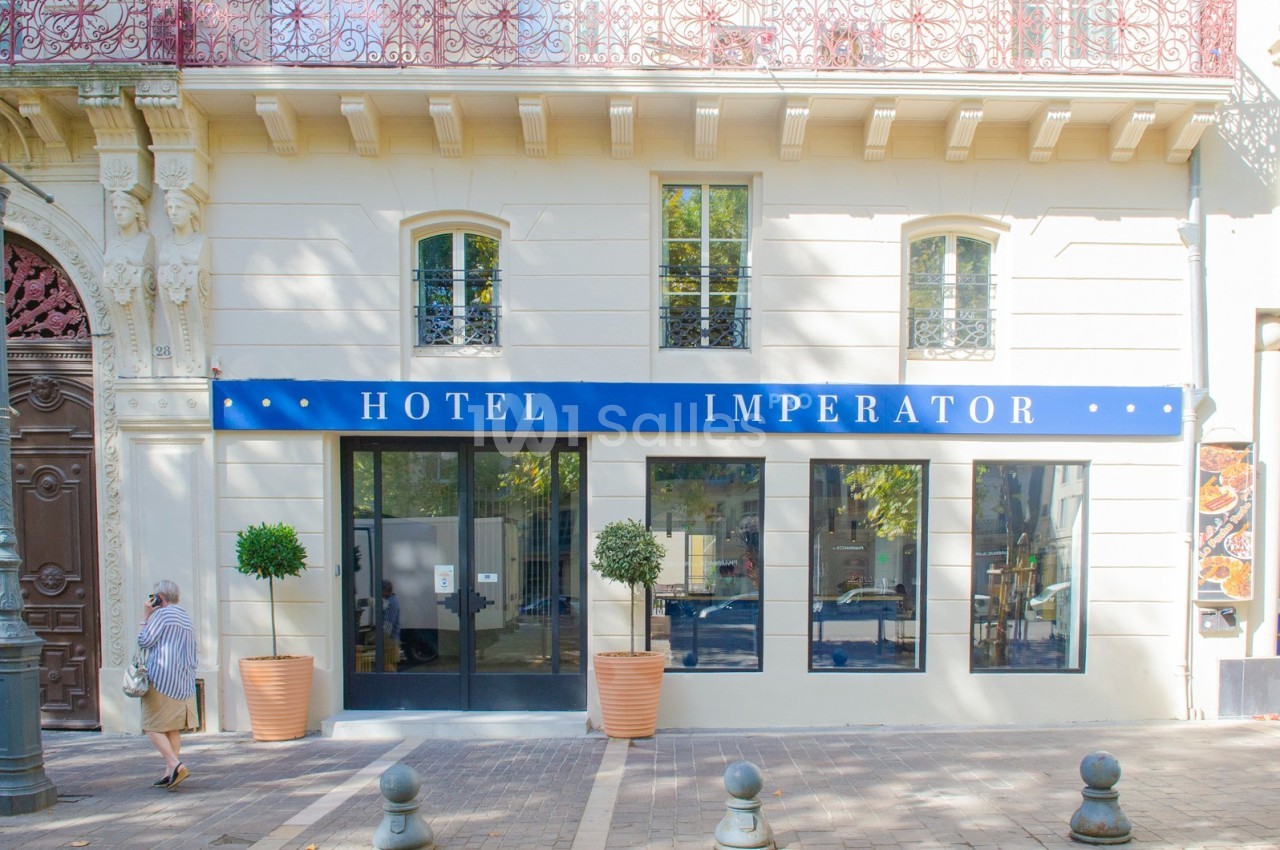 Façade d'un hôtel avec une enseigne bleue ’Hotel Imperator’, grandes fenêtres et deux arbres en pot devant l'entrée.