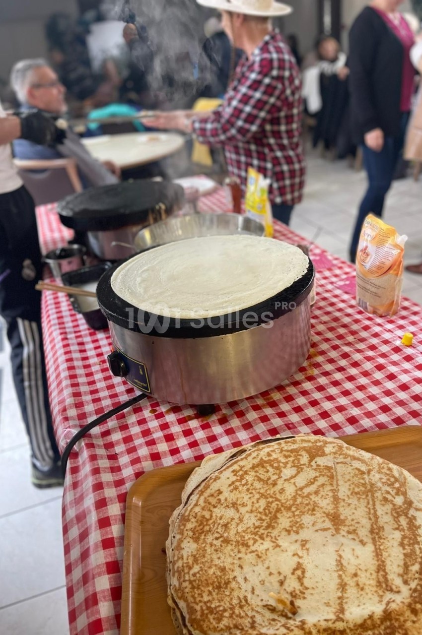 Crêpes en cours de préparation sur des crêpières électriques lors d'un événement convivial en intérieur.