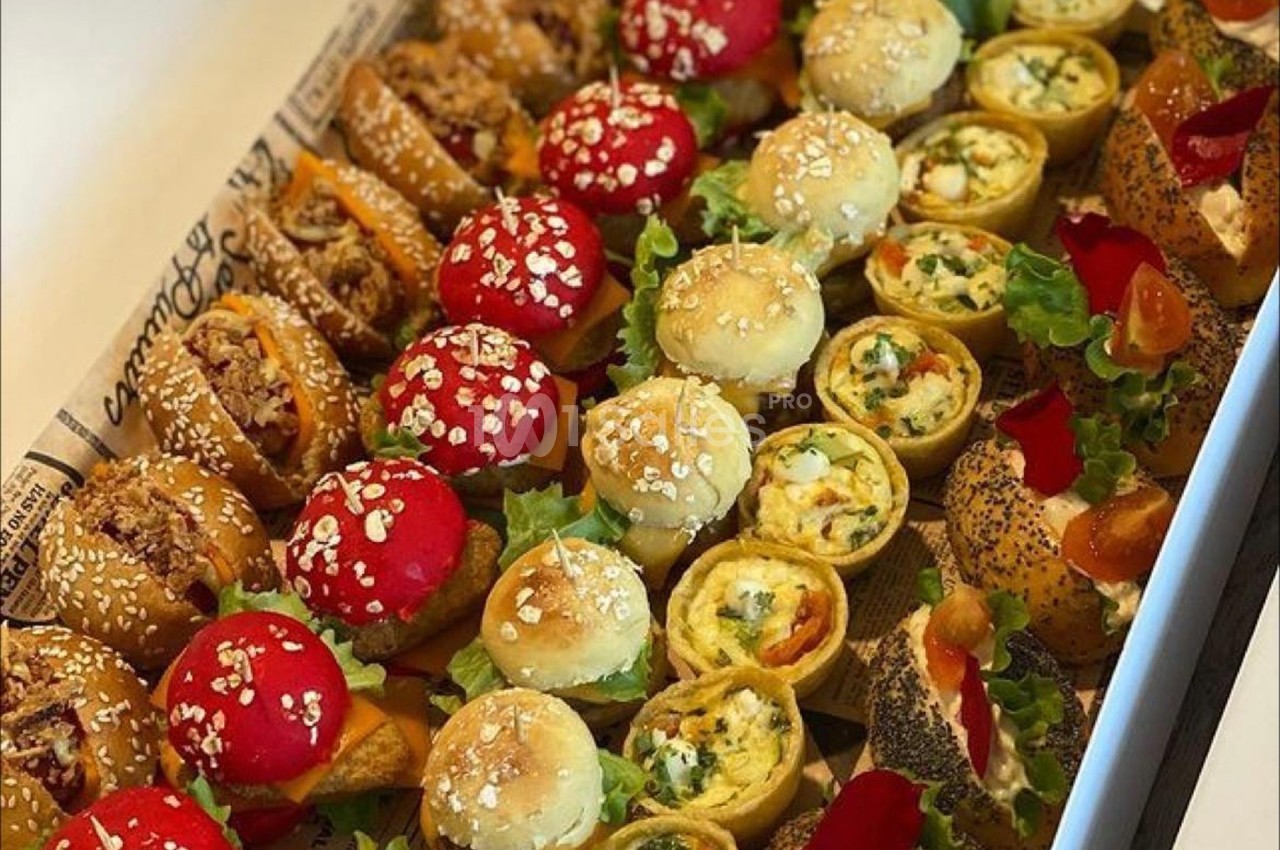 Plateau de bouchées variées comprenant mini-sandwichs, feuilletés et roulés garnis de légumes et graines.