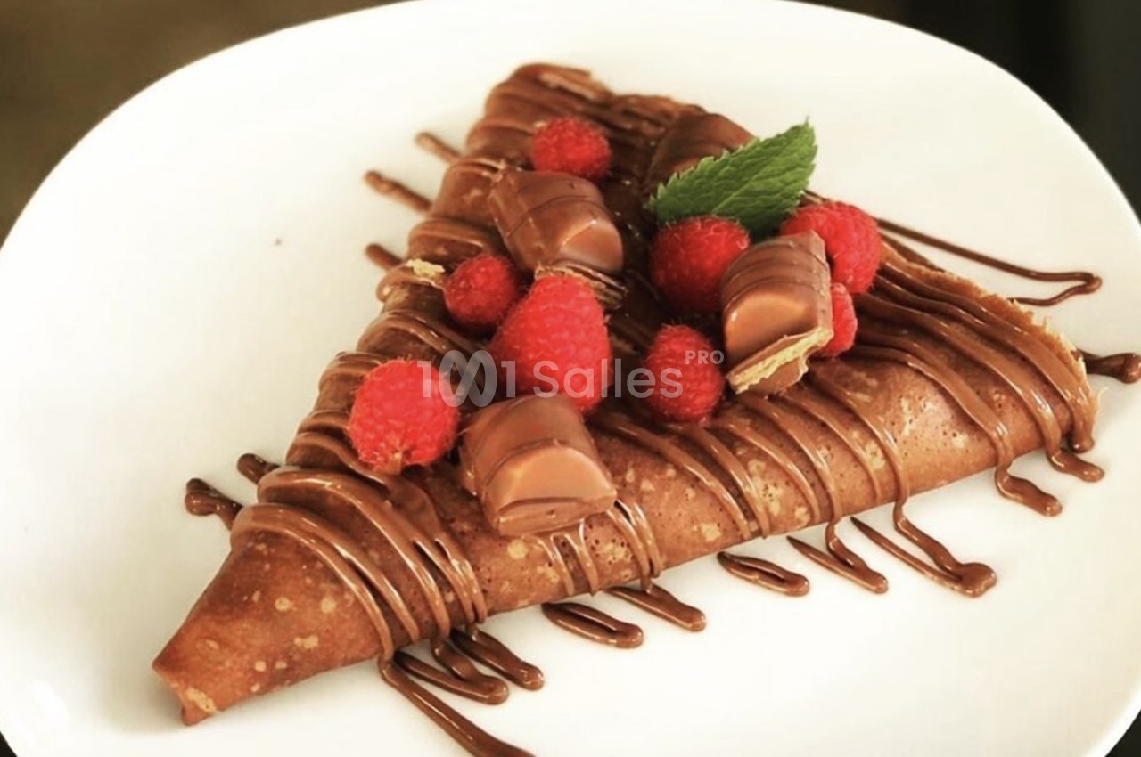 Crêpe garnie de chocolat, framboises fraîches et morceaux de chocolat, servie sur une assiette blanche.