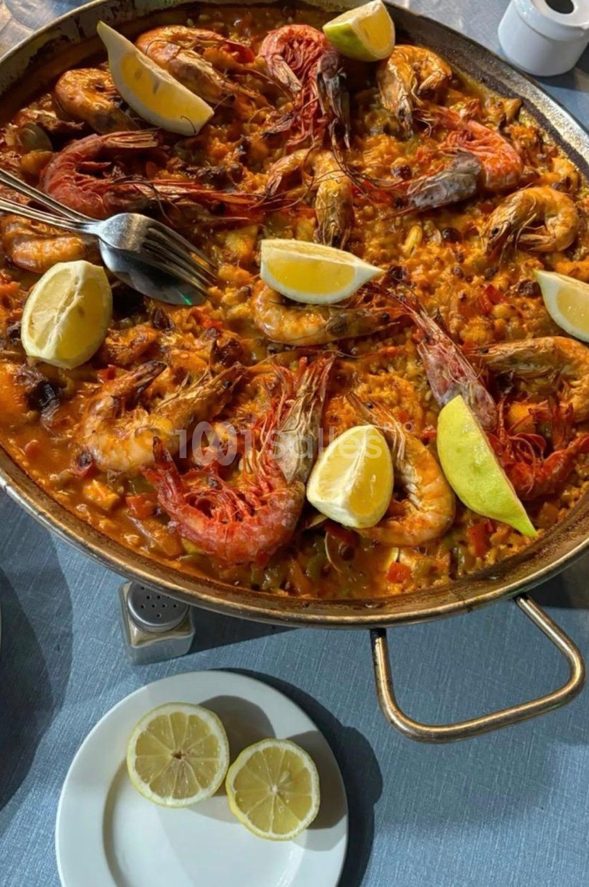 Plat de paella aux fruits de mer avec crevettes, citron et riz safrané, servi dans une grande poêle sur une table.