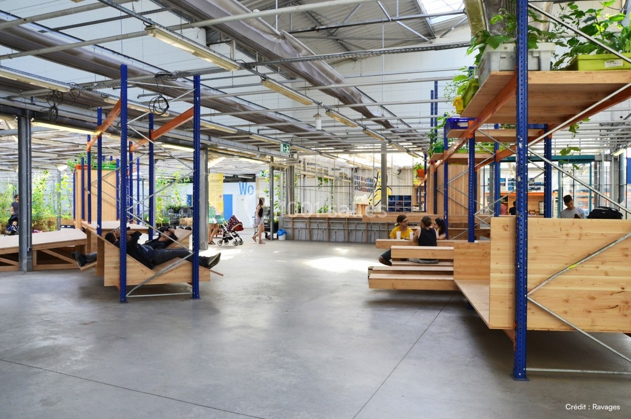 Espace intérieur lumineux avec structures en bois, plantes et personnes assises ou allongées dans un cadre ouvert et moderne.