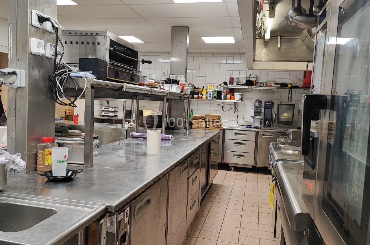 Cuisine professionnelle équipée avec plans de travail en inox, appareils de cuisson et étagères de rangement.