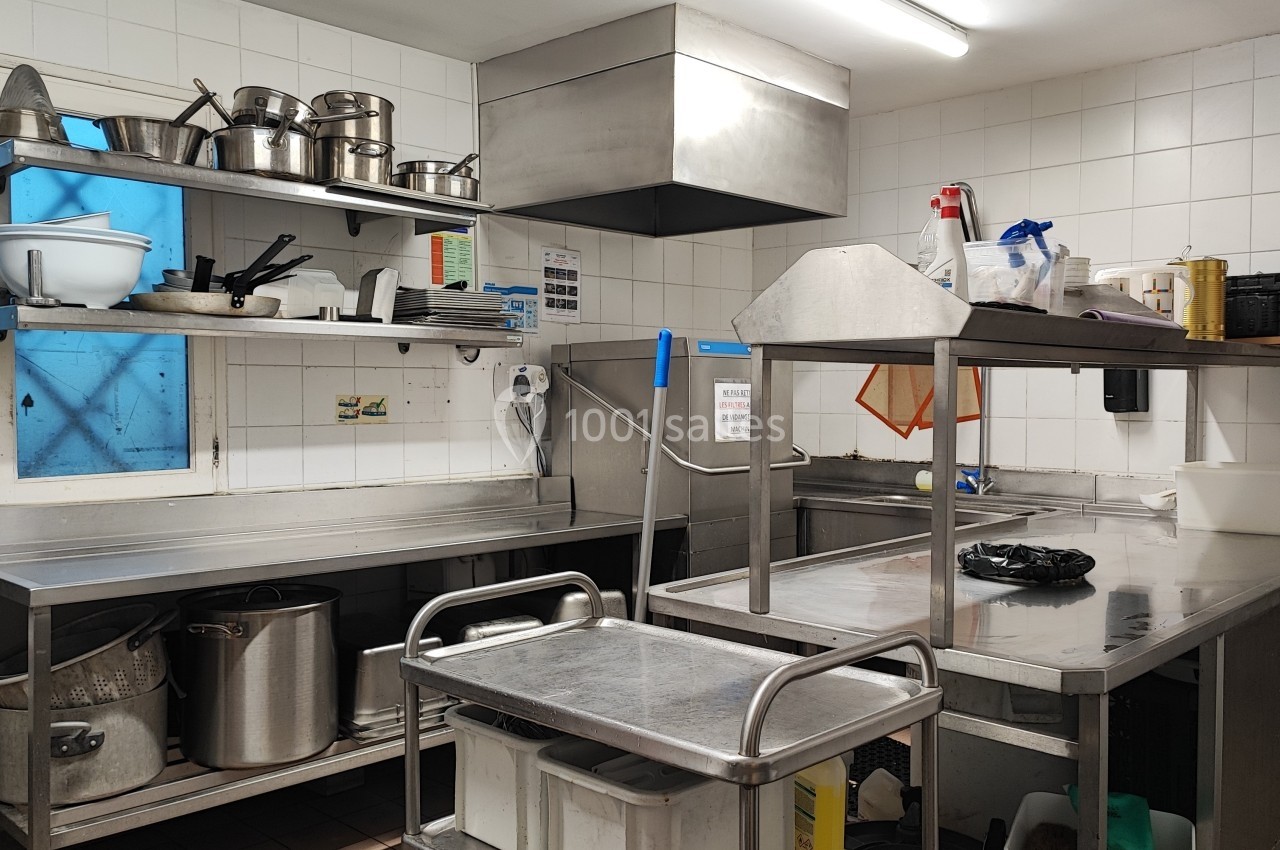 Cuisine professionnelle avec plans de travail en inox, étagères garnies d'ustensiles et équipements de nettoyage.