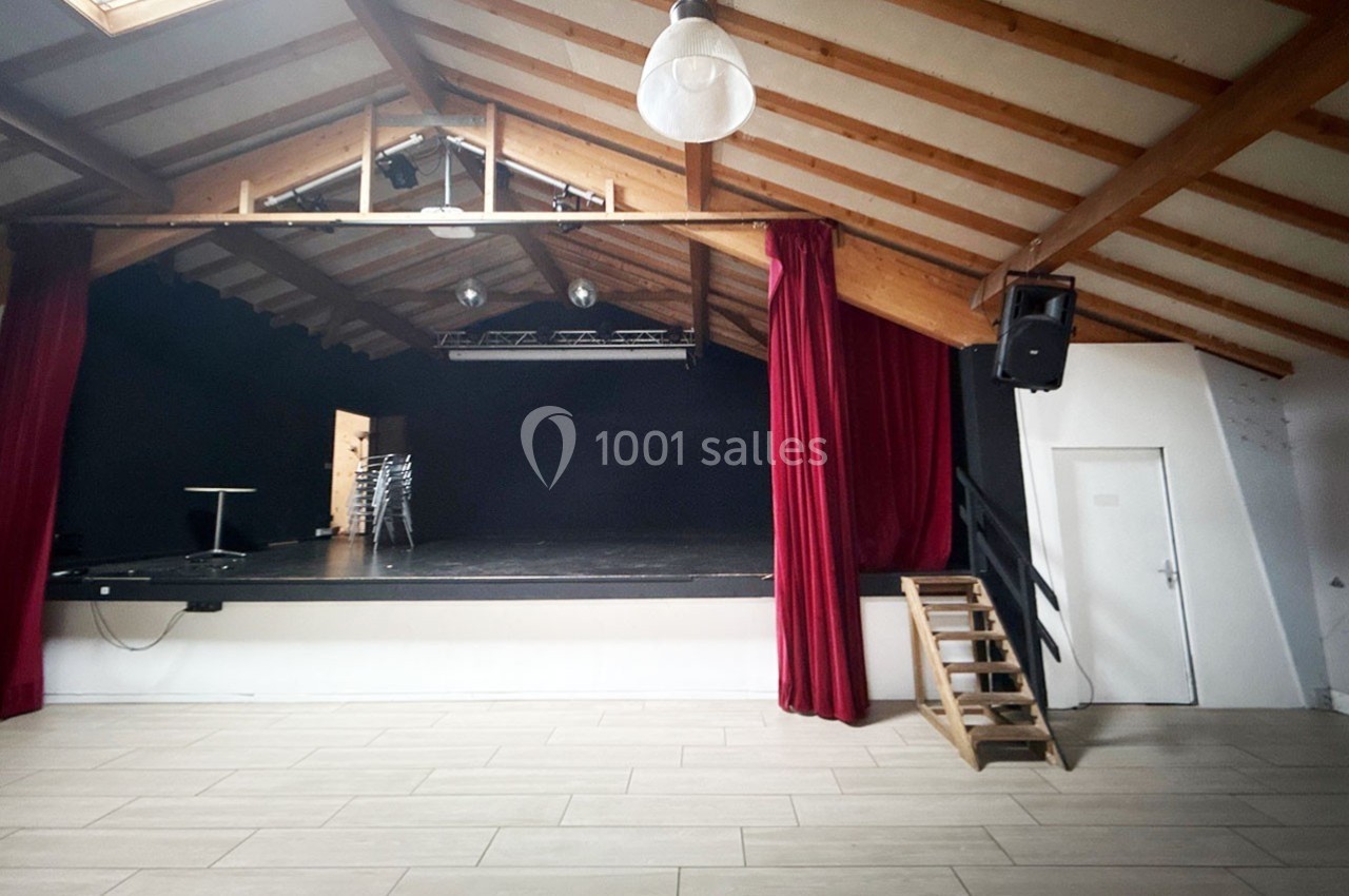 Scène surélevée dans une salle avec plafond en bois, rideaux rouges et éclairage suspendu.