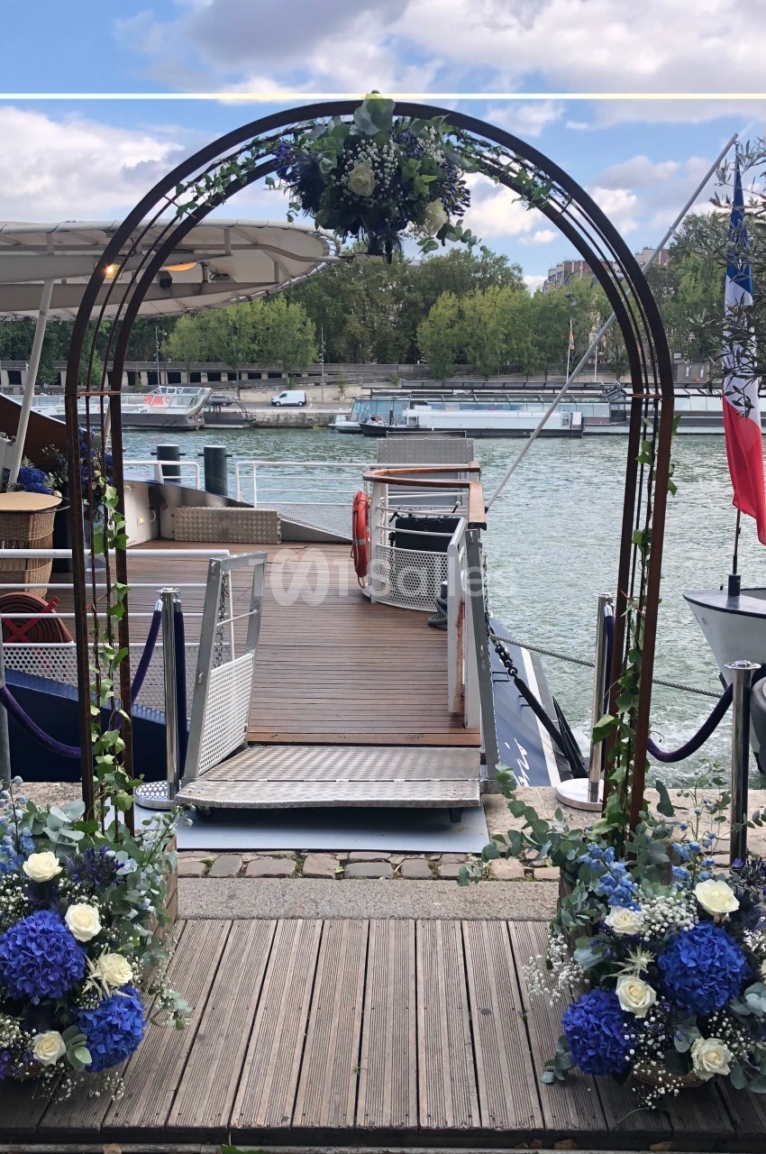 Arche décorée de fleurs bleues et blanches, installée près d'un ponton au bord d'une rivière.
