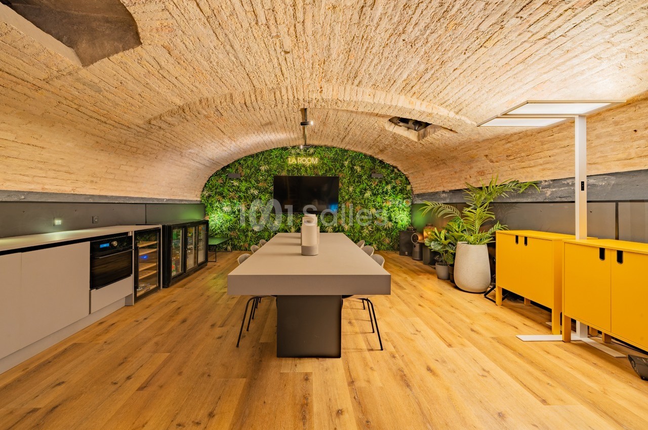 Salle de réunion voûtée avec mur végétal, table centrale, chaises, rangements et éclairage moderne.