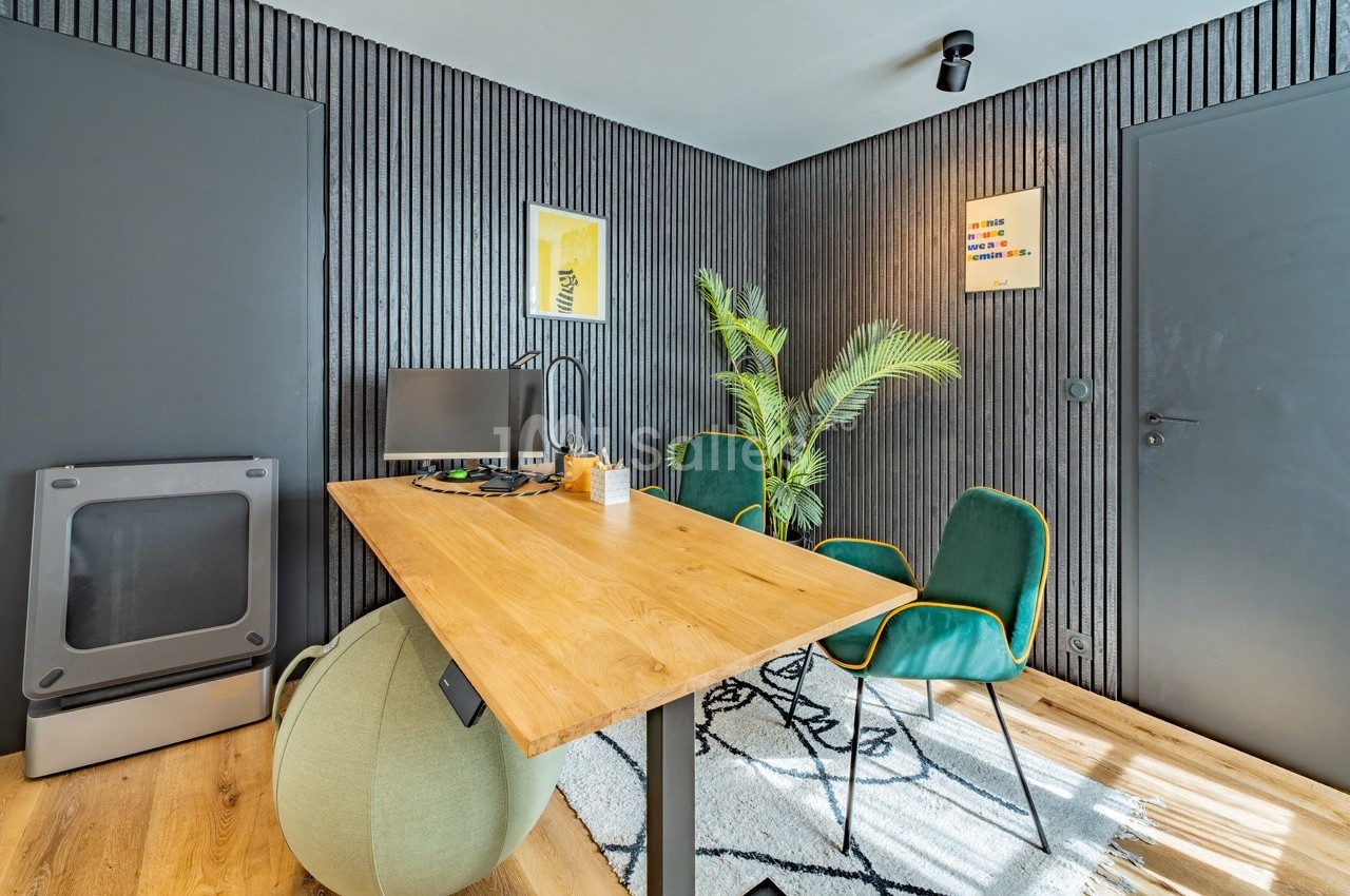 Bureau moderne avec table en bois, chaise, écran d'ordinateur, plantes vertes et murs noirs texturés.