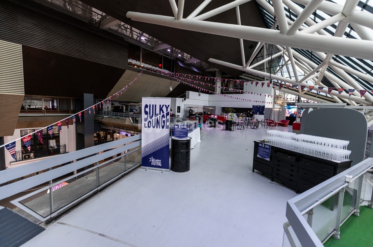 Espace intérieur lumineux avec des tables, des chaises, des guirlandes et un panneau indiquant ’Sulky Lounge’.