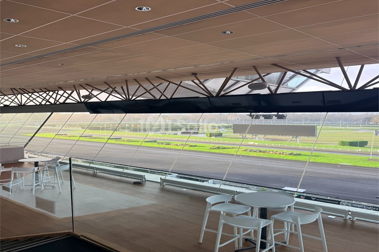 Vue intérieure d'une salle avec baies vitrées donnant sur une piste extérieure et des espaces verts.
